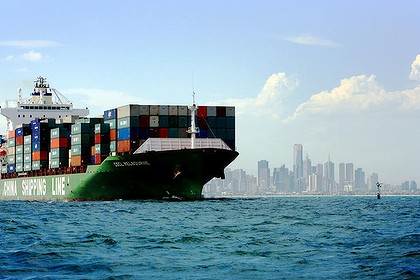 huge modern containership full of cargo with a city's silhouette in the background