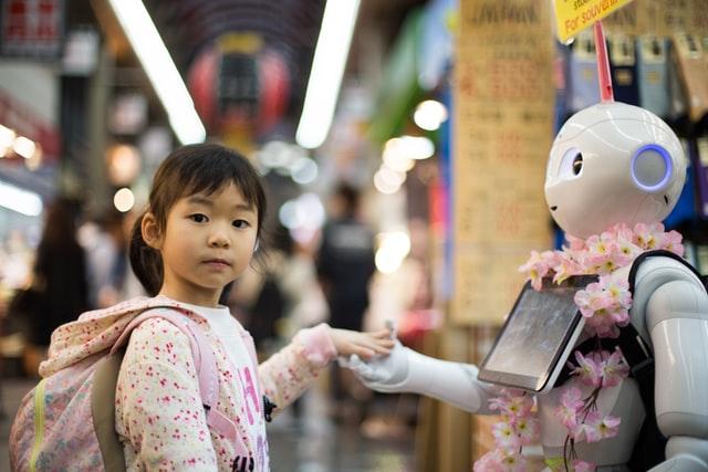 Young girl holds hands with a robot at a market.