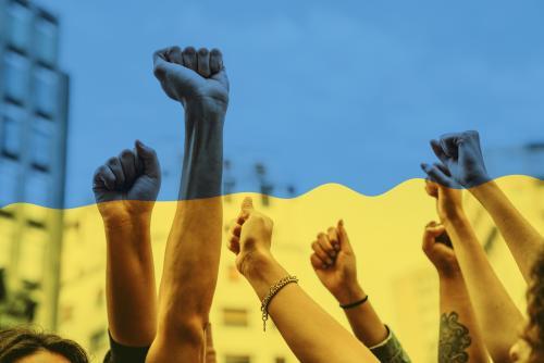 Several fists raised toward the sky, overlaid with the Ukrainian flag