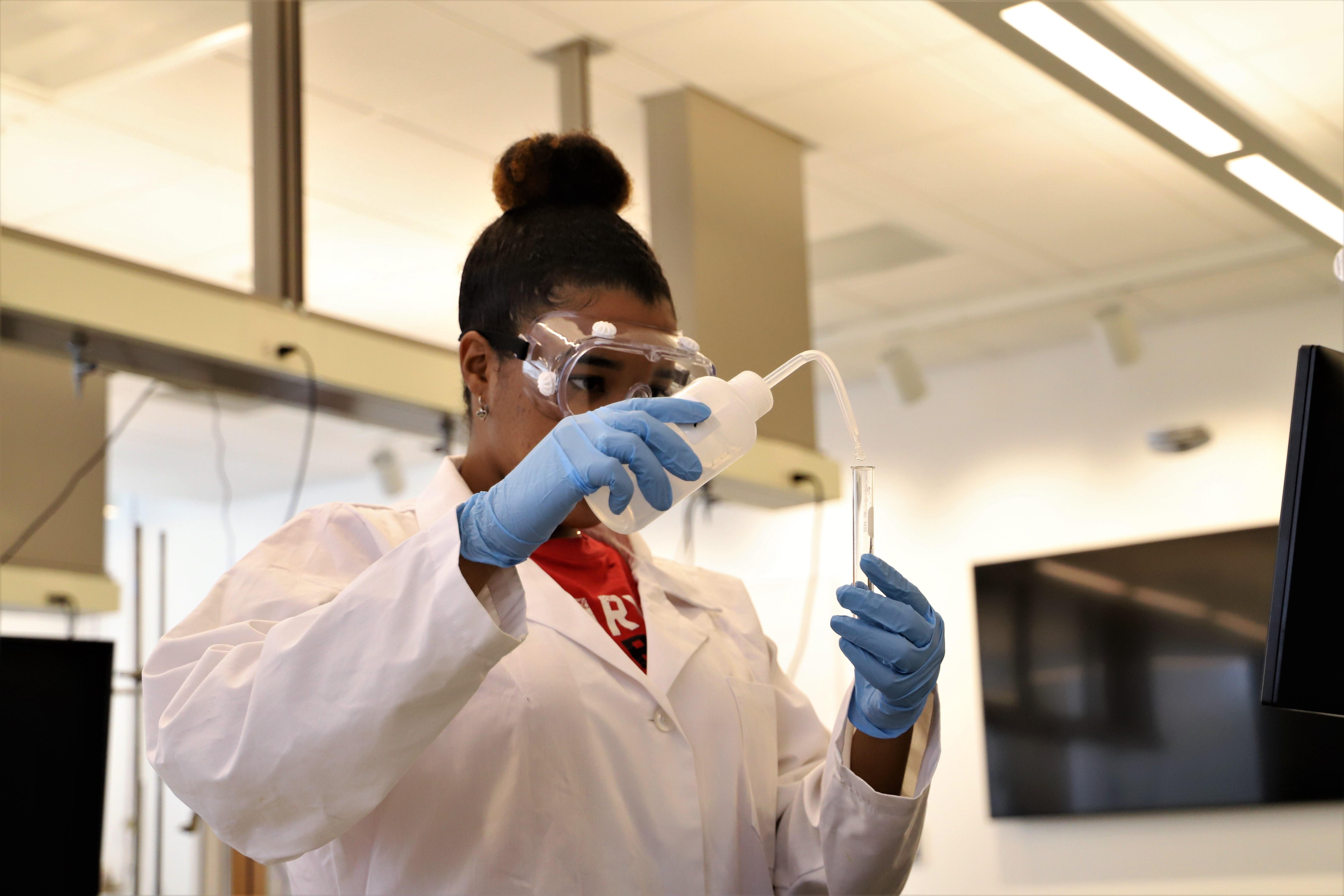 Undergraduate student in lab coat and safety goggles using lab equipment