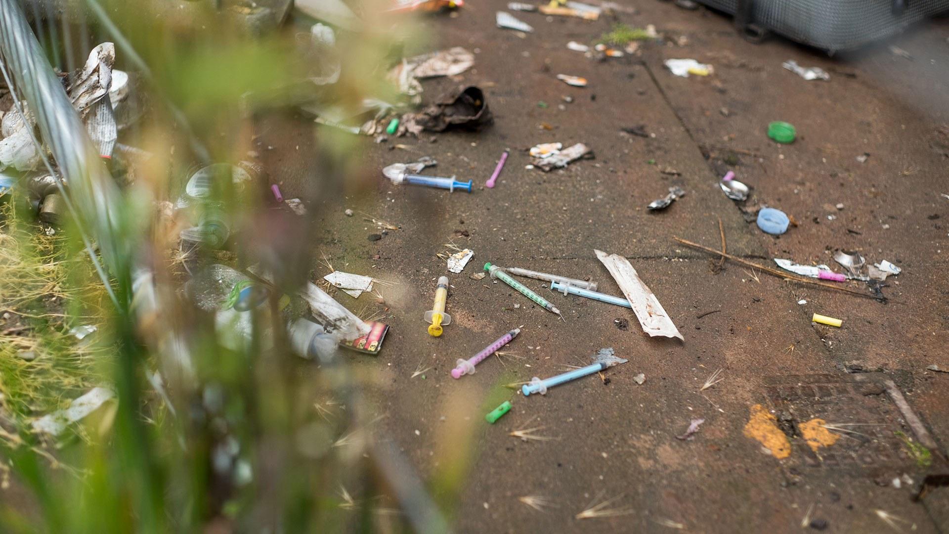 Needles and trash scattered across concrete ground