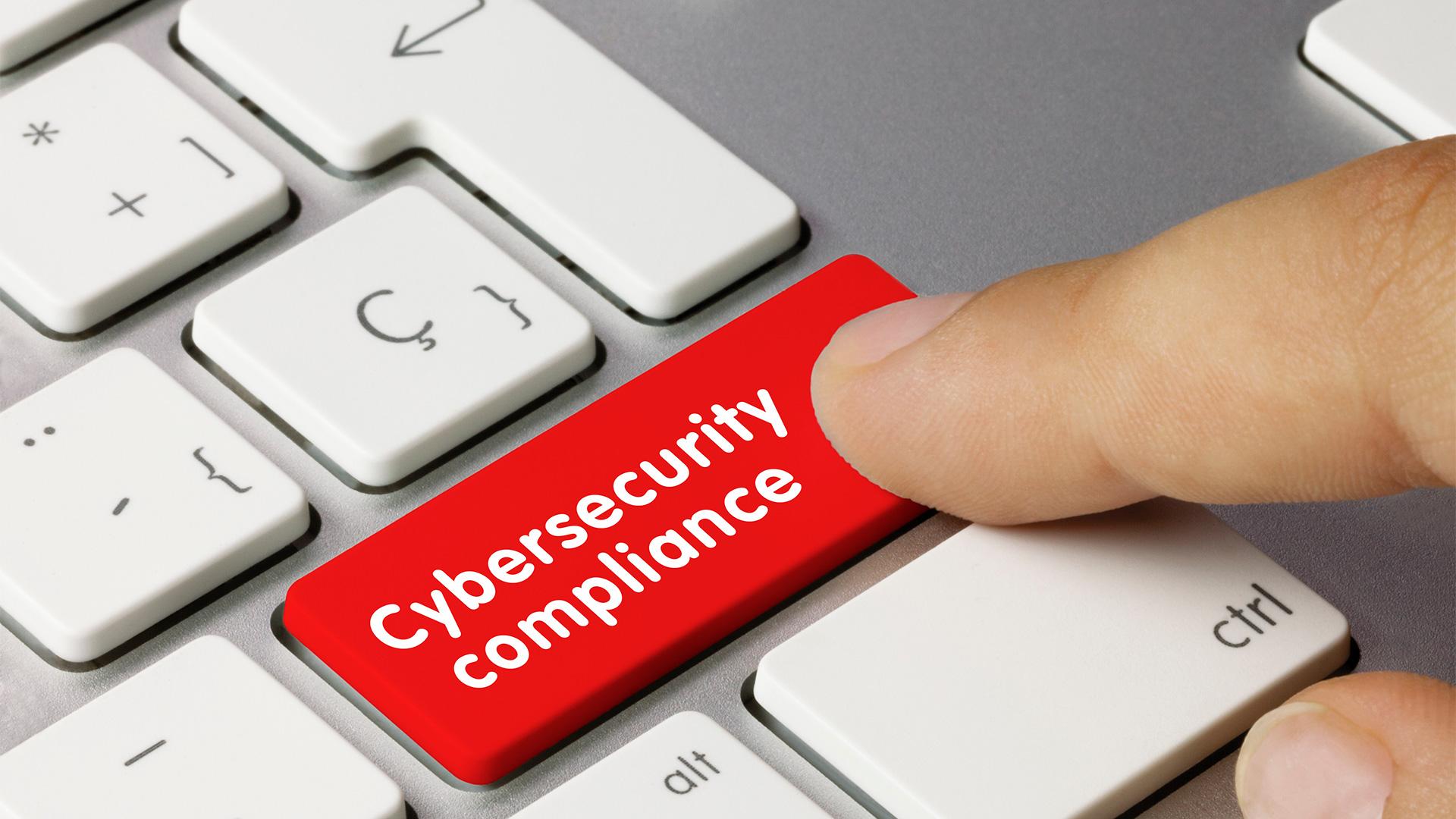 Hand pressing red button on keyboard labeled "cybersecurity compliance"
